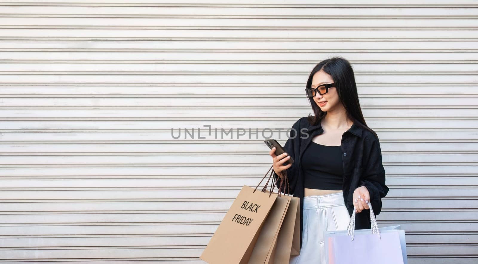 Asian woman using smartphone and looking away while enjoying a day shopping. Black Friday sale and discount. Buying clothes presents for holidays.