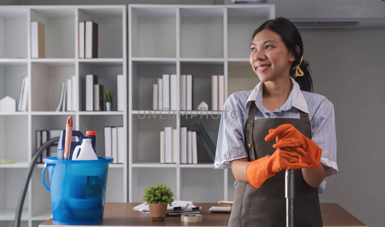 Portrait of a beautiful young housewife smiling and happy, holding cleaning supplies in the office. cleaning supplies, housekeeper.