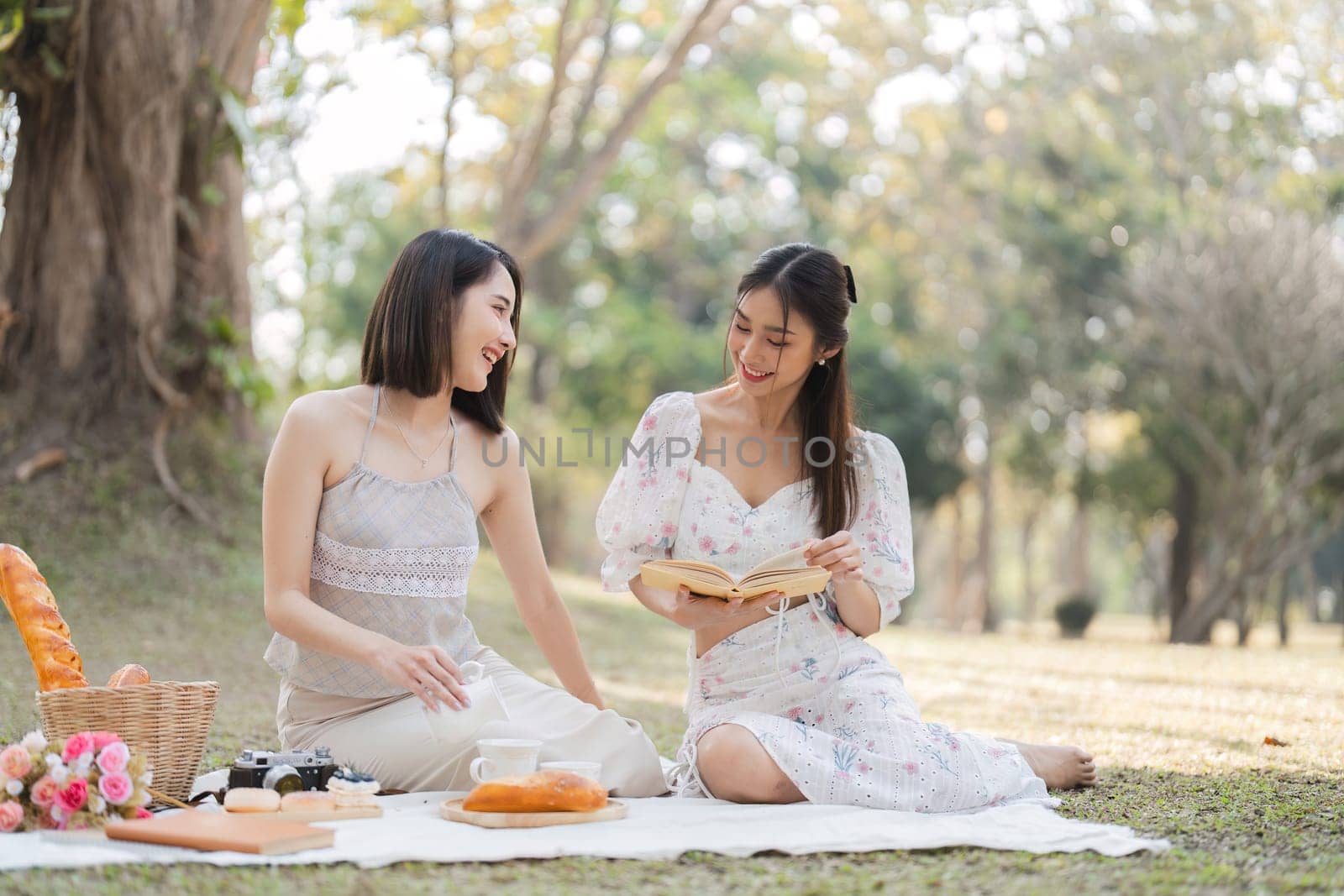 Two beautiful LGBT young women in casual clothes and summer hats Carefree woman having a picnic outside Positive model sitting on the grass eat fruit and cheese Take a selfie. LGBT concept.