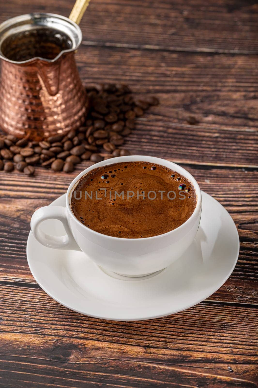 Double Turkish coffee in a white porcelain cup with a decorative coffee pot on a wooden table by Sonat