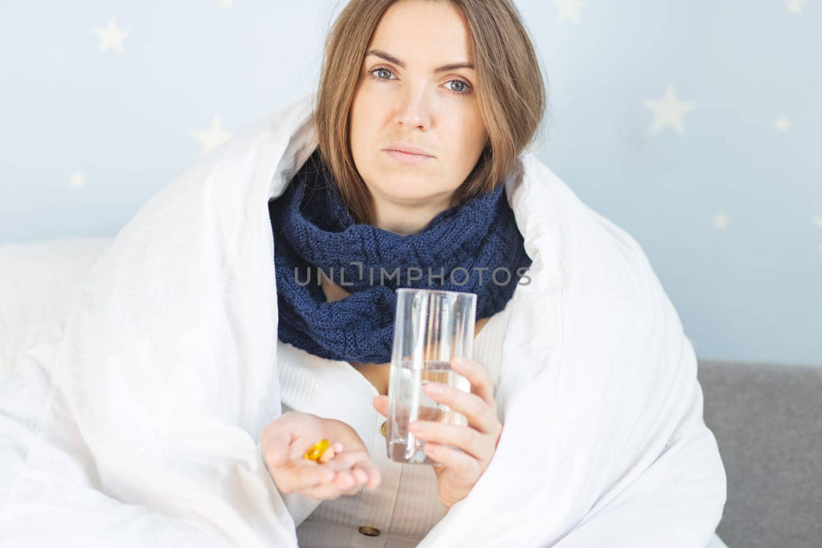 Influenza treatment or coronavirus . Flu-sick woman, wrapped in warm scarf and blanket , taking pills holding glass of water.