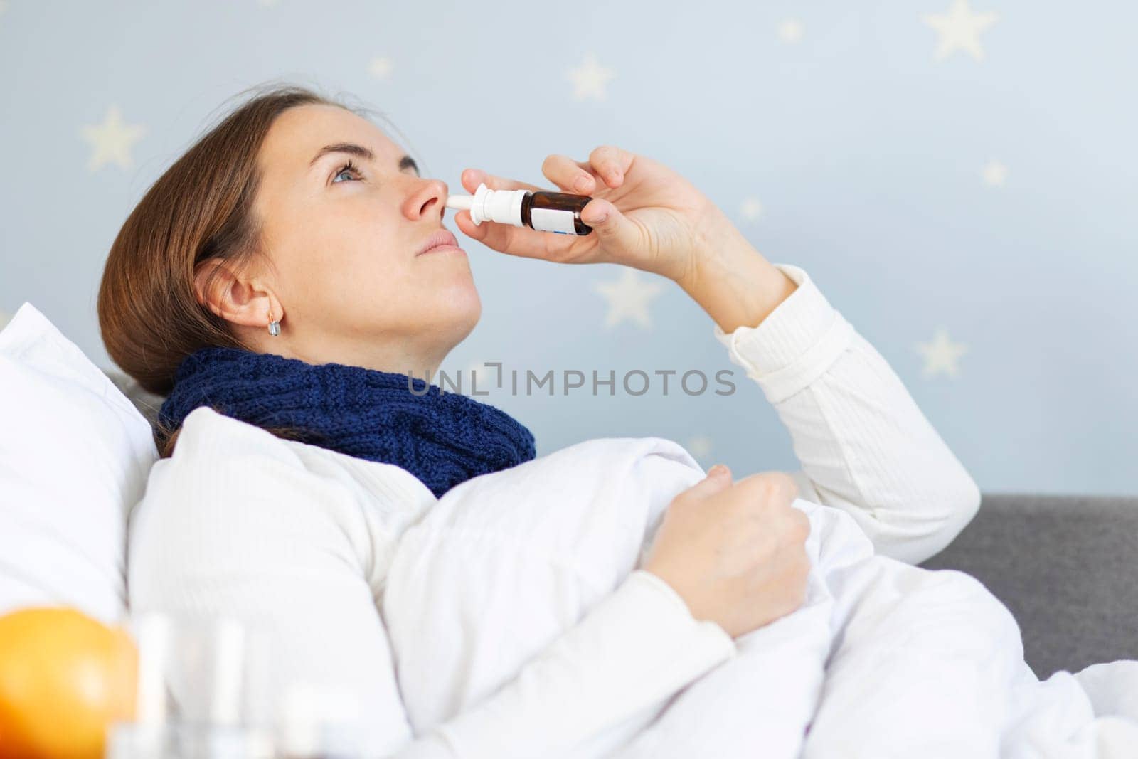 A young woman with bad cold lying in bed under the blanket and using nasal drops. Woman using nose spray.