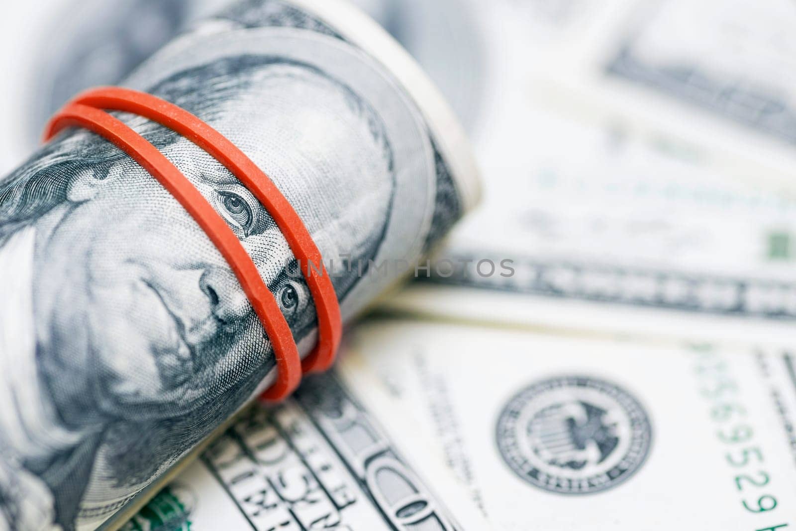 A roll of 100 dollar bills close-up on a pile of American dollars. Background from banknotes of 100 american dollars. Financial concept.