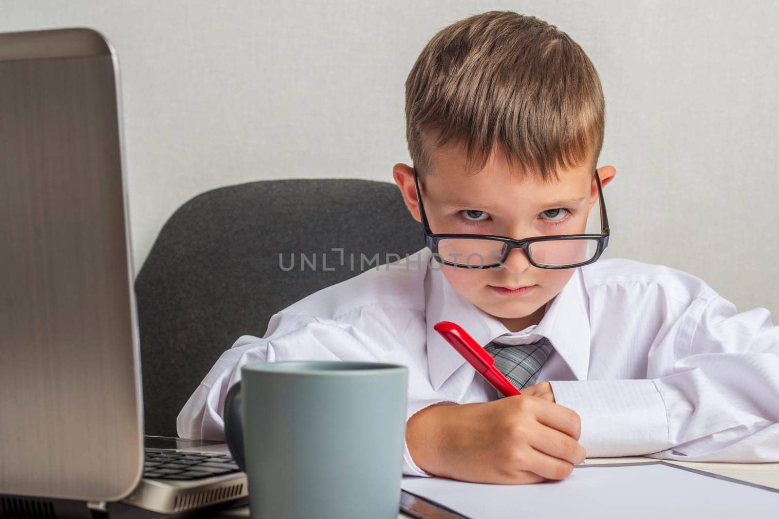 Little boss in the office. A kid businessman with glasses working with documents in office.