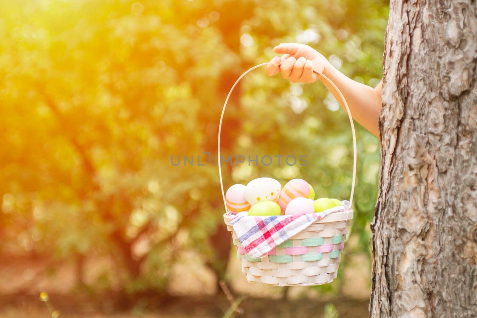 Childrens hand holding basket with colorful easter eggs in garden or park. Happy Easter background. Copy space for text.