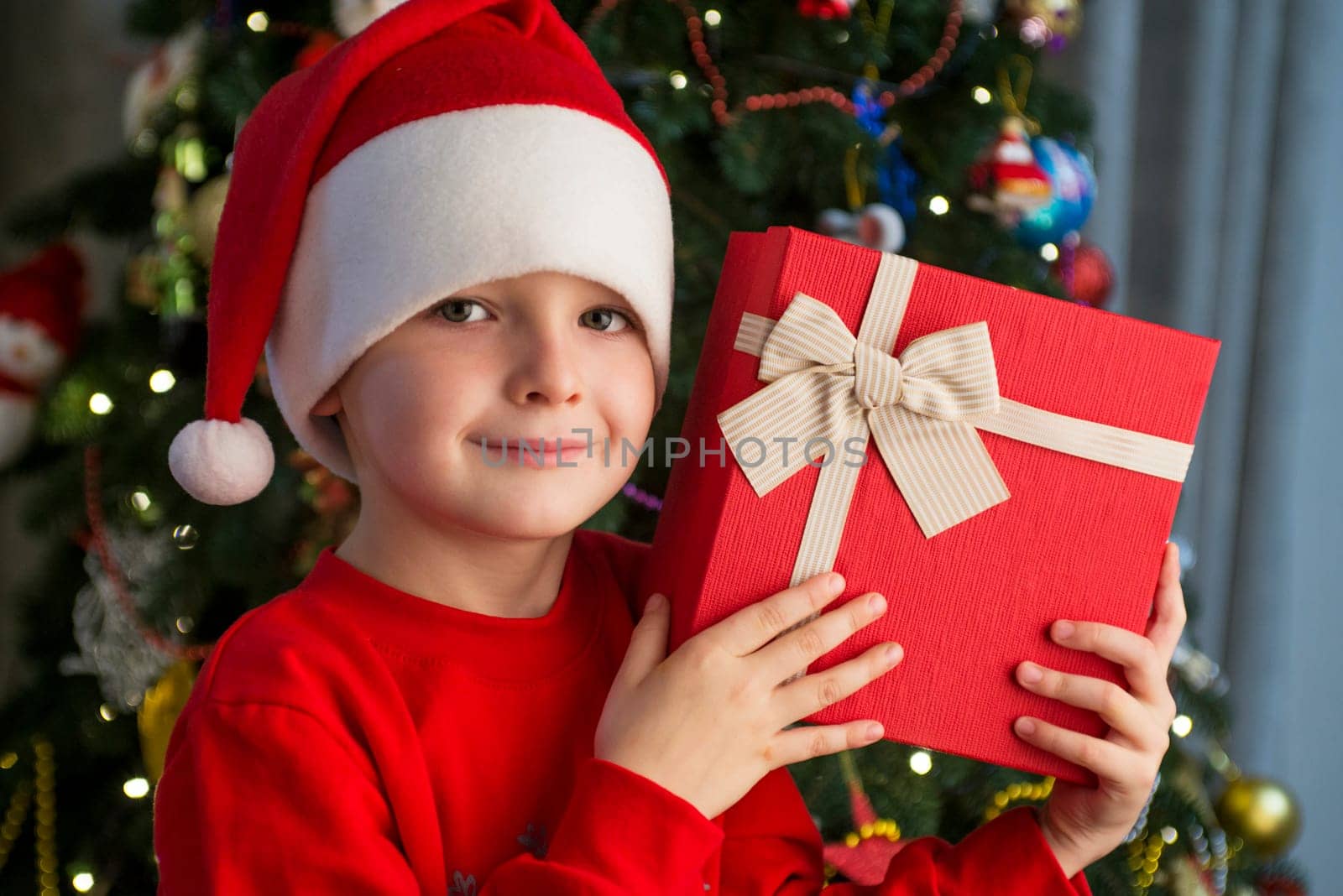 Child near Christmas tree with gift box. Cute little boy is standing near Christmas tree with gift. Merry Christmas and Happy New Year.