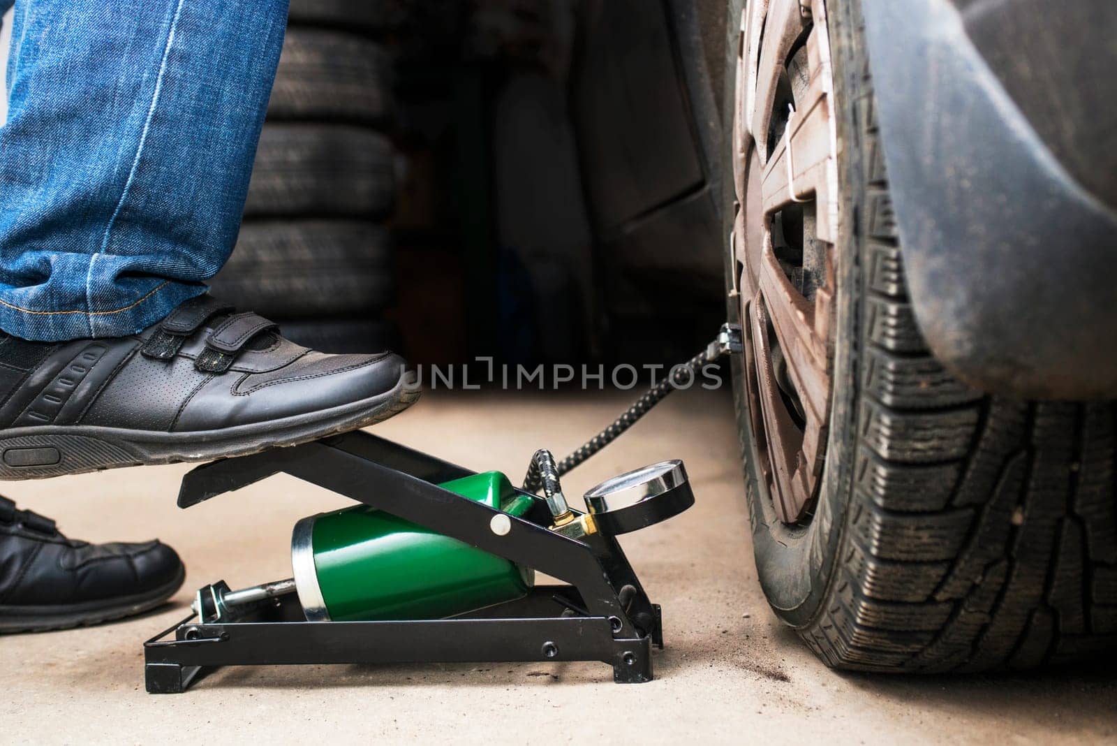 Man's foot pumping up a flat car tyre or tire, which is deflated. Man Inflating car tyre with foot pump. Concept of checking a car before traveling .