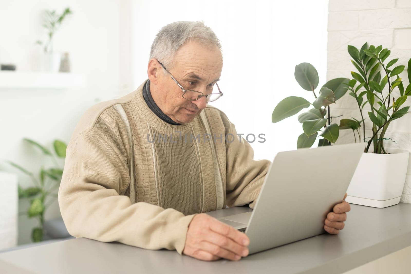 Senior man with eyeglasses connected with laptop at home. by Andelov13