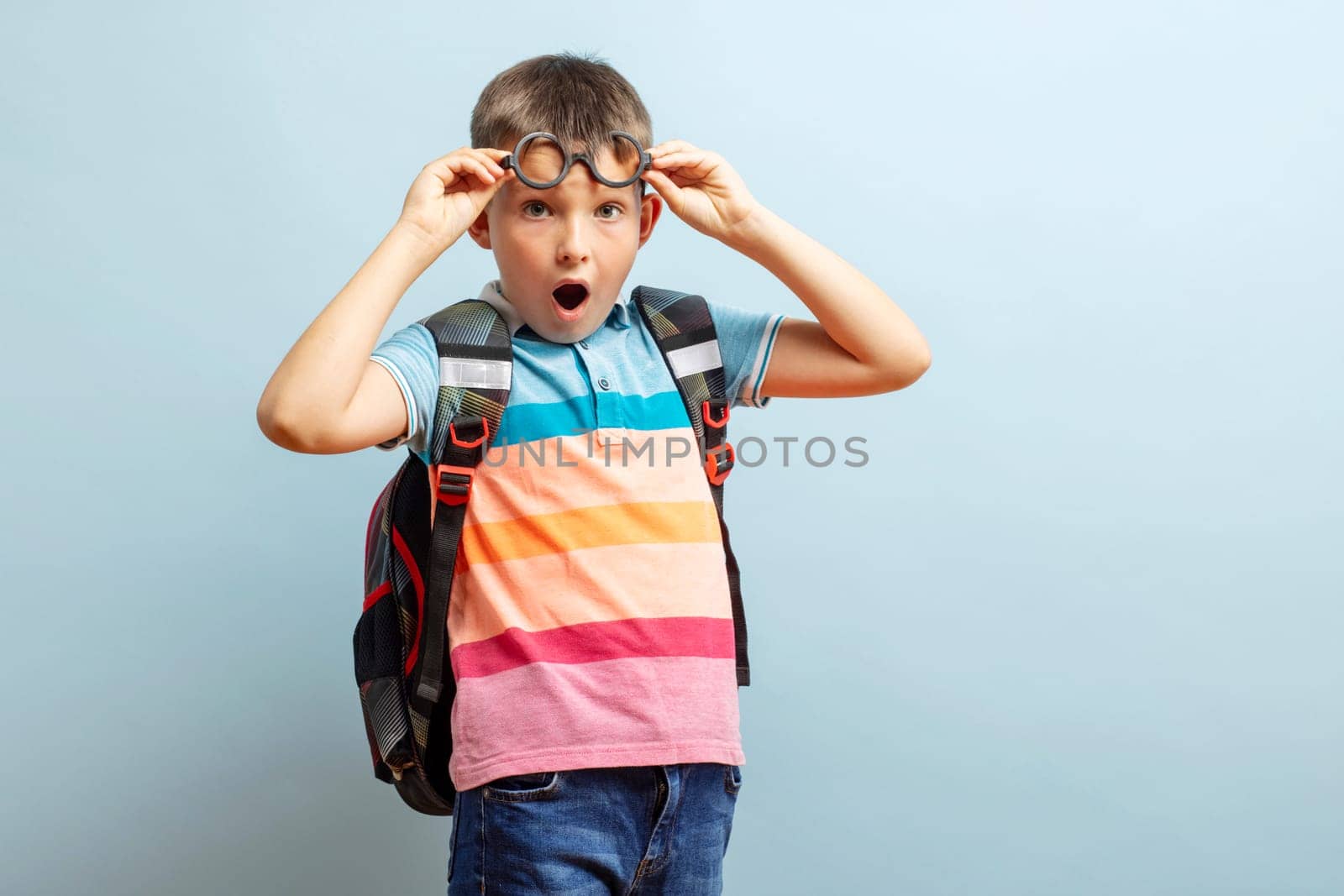 Surprised schoolboy in glasses with backpack on blue background. Back to school.