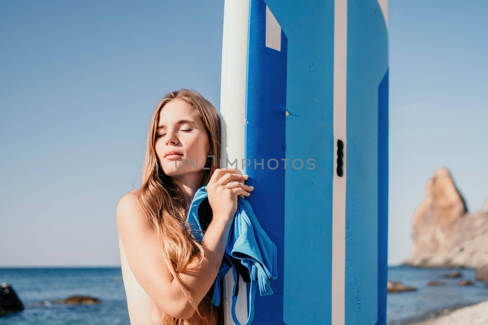 Woman sea sup. Close up portrait of happy young caucasian woman with long hair looking at camera and smiling. Cute woman portrait in a blue bikini posing on sup board in the sea by panophotograph