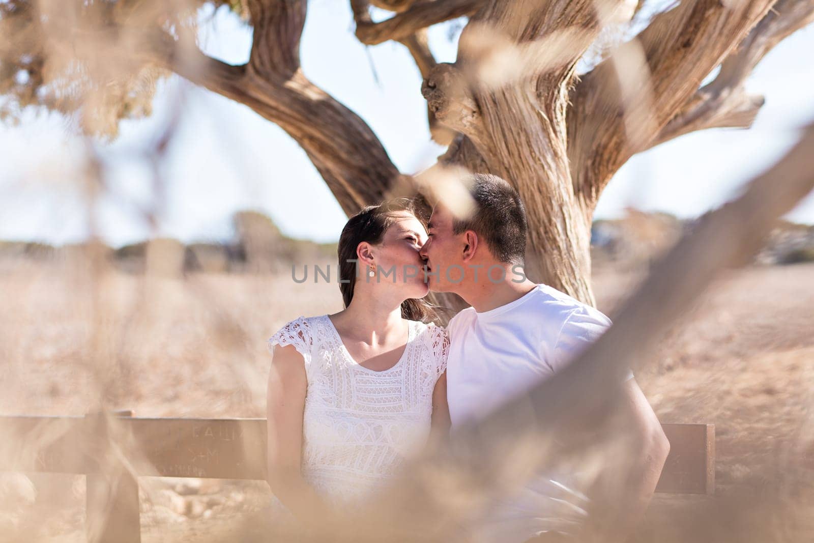 happy young couple kissing and hugging, sitting under the tree