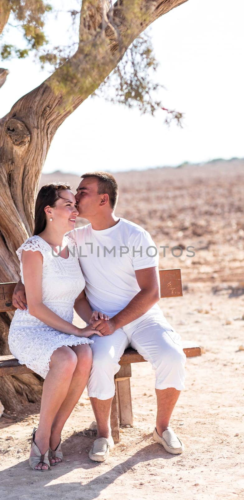 happy young couple kissing and hugging, sitting under the tree