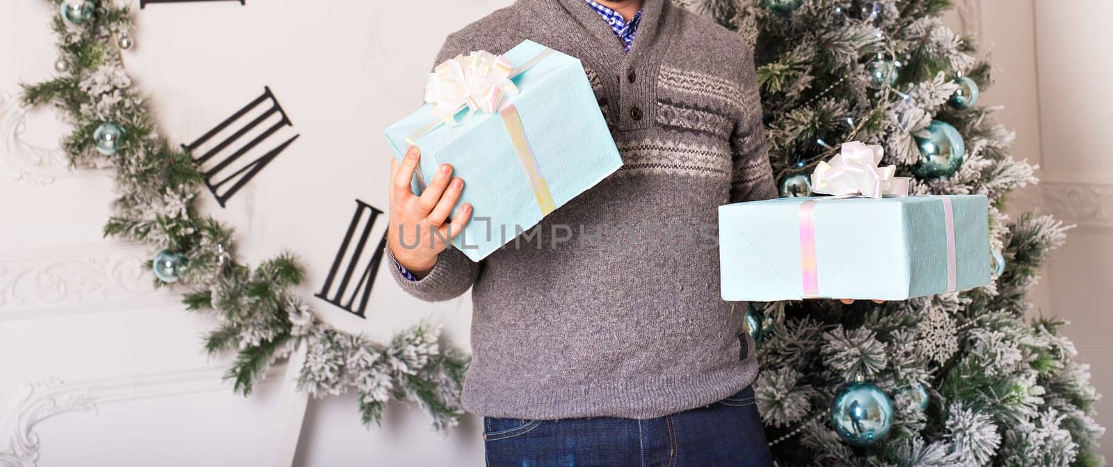 Young man holding gifts in front of Christmas tree.
