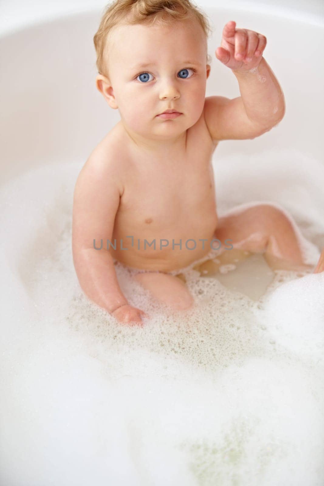 Baby, face and hand in bubble bath or water cleaning for skin or hair wash for childhood development, hygiene or soap. Child, boy and point in tub for question or confused for cleansing, foam in home.