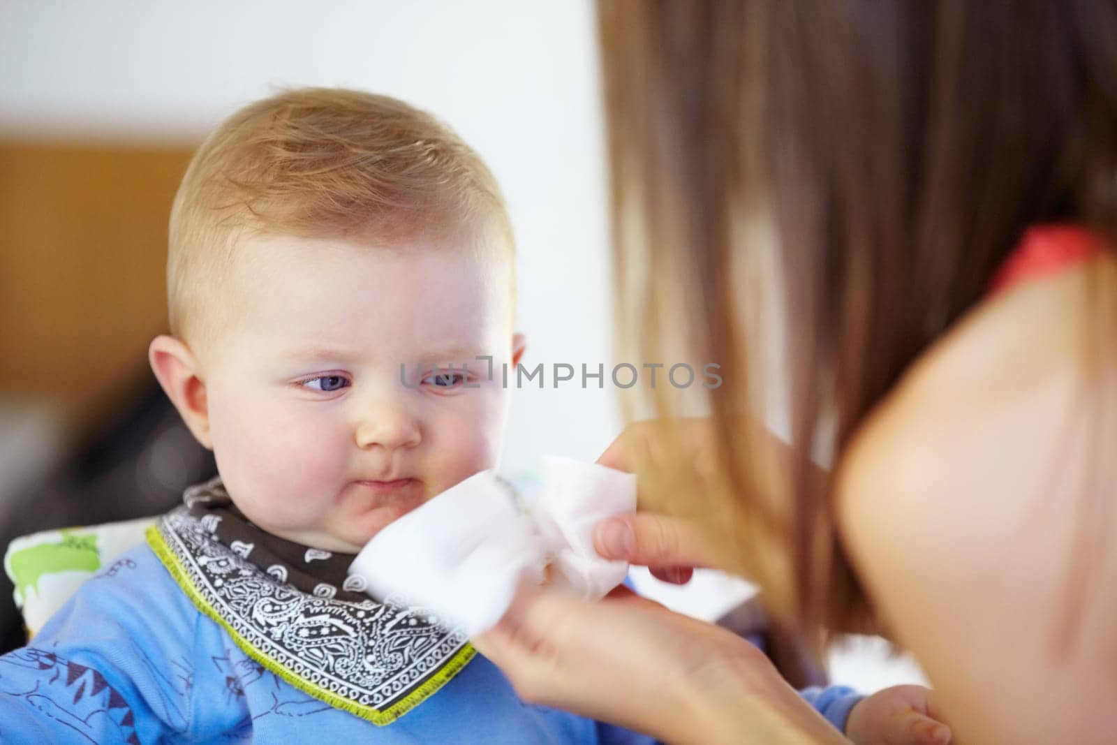 Woman, baby and wipe of mouth for eating, delicious and food for breakfast in kitchen. Little boy, toddler and looking at mother for clean up of yummy, meal or snack for hunger with napkin for mess.