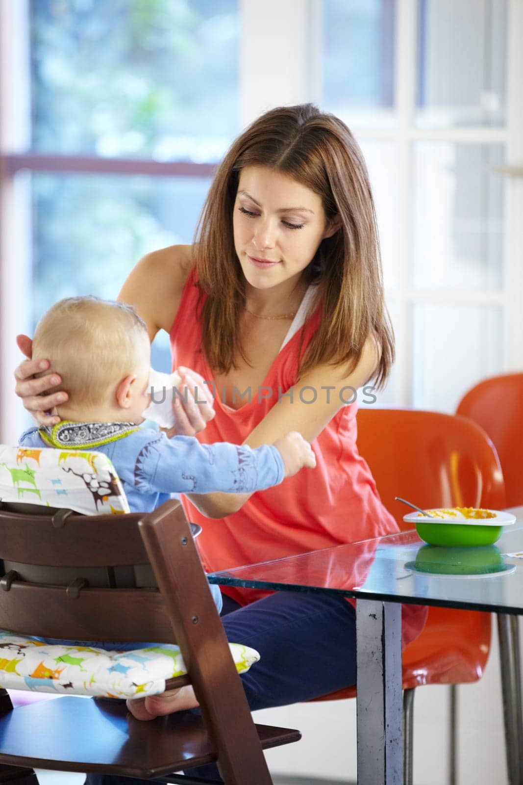 Mother, baby and food in feeding chair for nutrition, growth and development at table in kitchen of home. Woman, infant and cleaning face after eating, napkin and routine for love, care and nurture by YuriArcurs