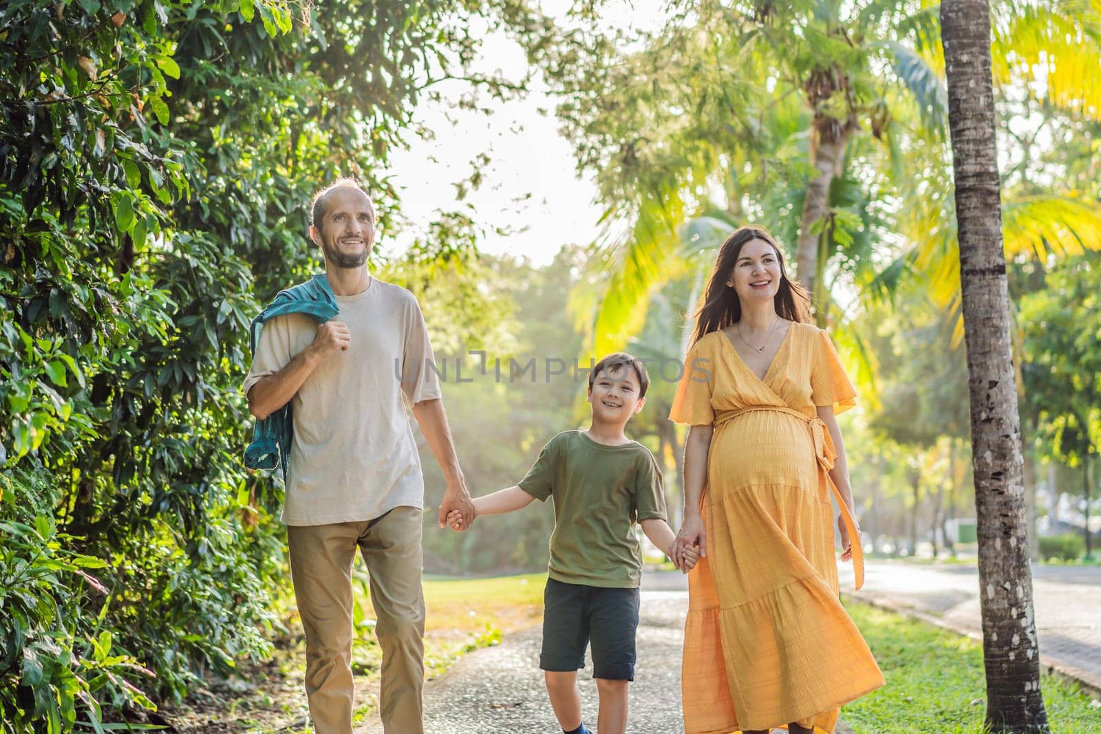 A loving family enjoying a leisurely walk in the park - a radiant pregnant woman after 40, embraced by her husband, and accompanied by their adult teenage son, savoring precious moments together amidst nature's beauty. Pregnancy after 40 concept.