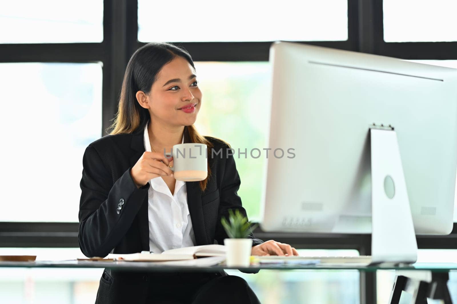 Attractive businesswoman holding coffee cup analyzing marketing data, statistics on computer screen.