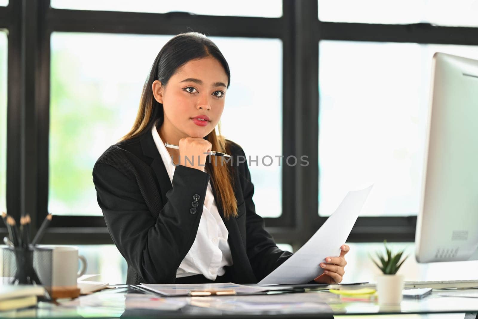 Professional asian female company manage wearing suit sitting at desk and looking at camera.