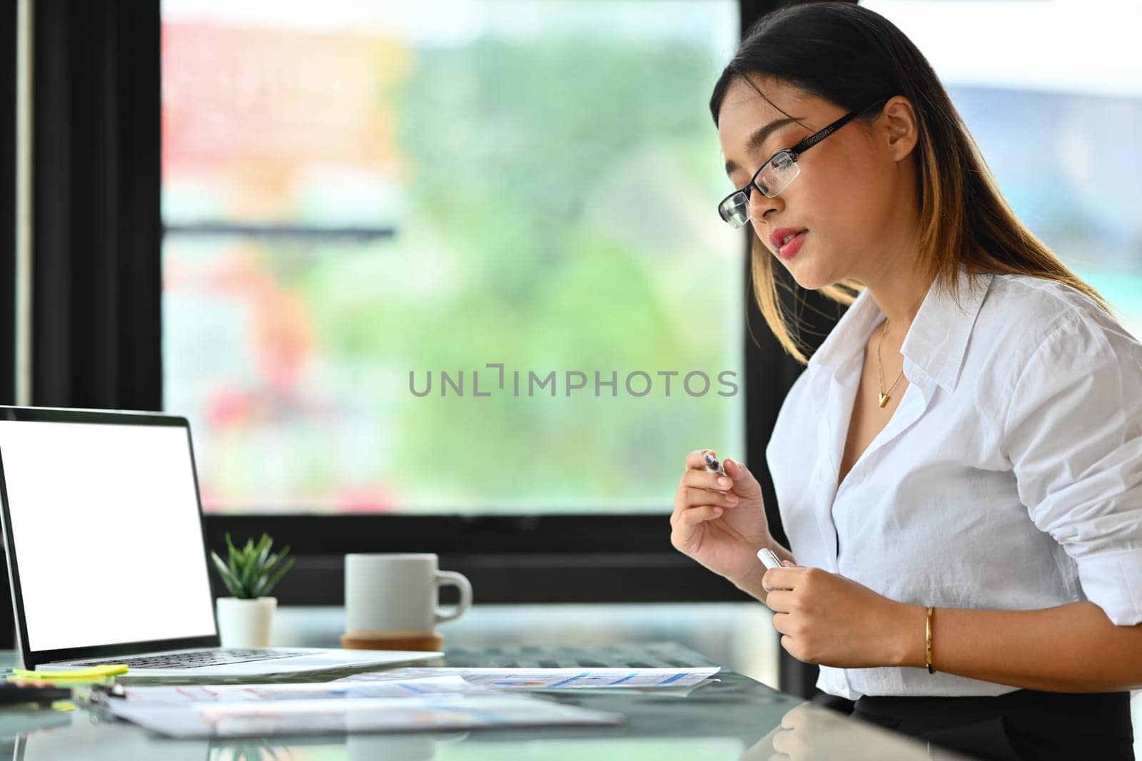 Beautiful female entrepreneur in glasses working on sale marketing project at modern workplace.
