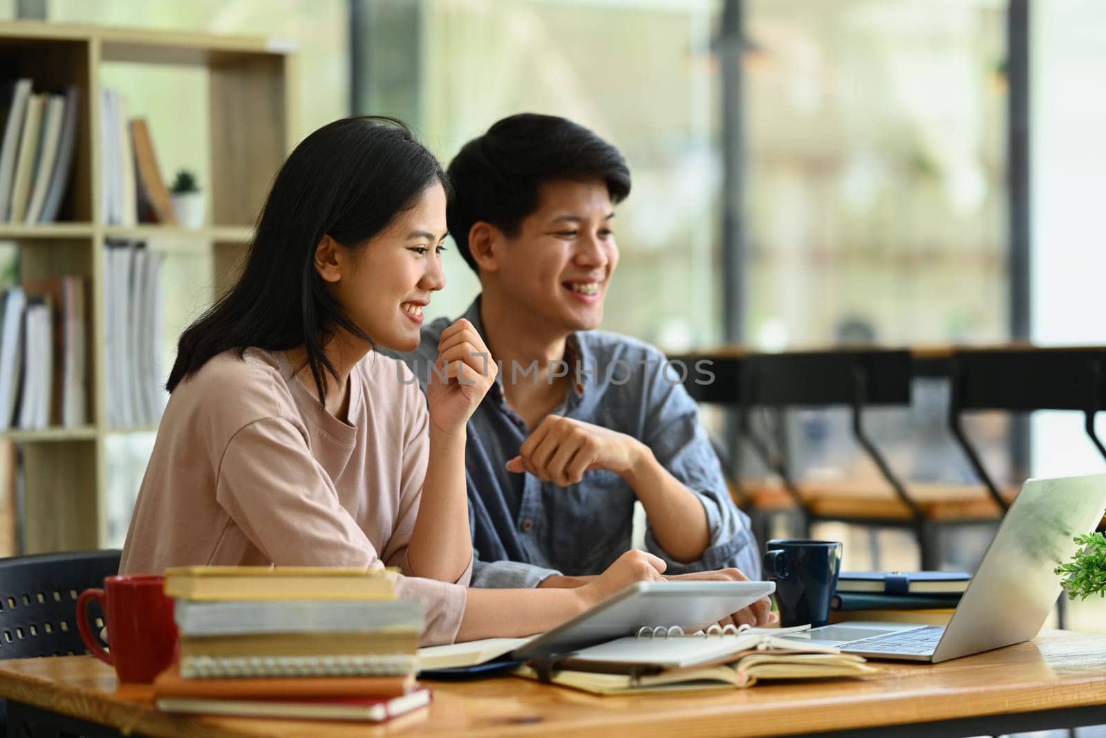 Cheerful male and female students discussing homework, brainstorming on common studying project in library by prathanchorruangsak