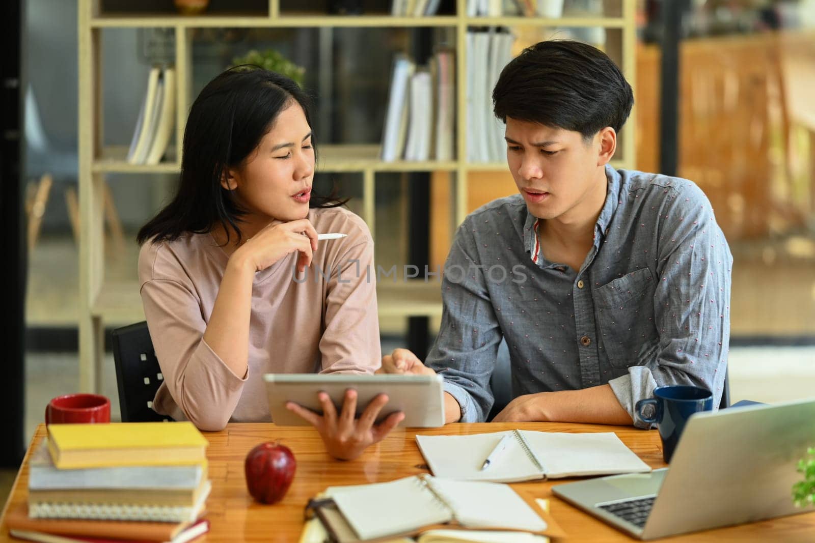 University students sitting at table with books and laptop preparing for exams together by prathanchorruangsak