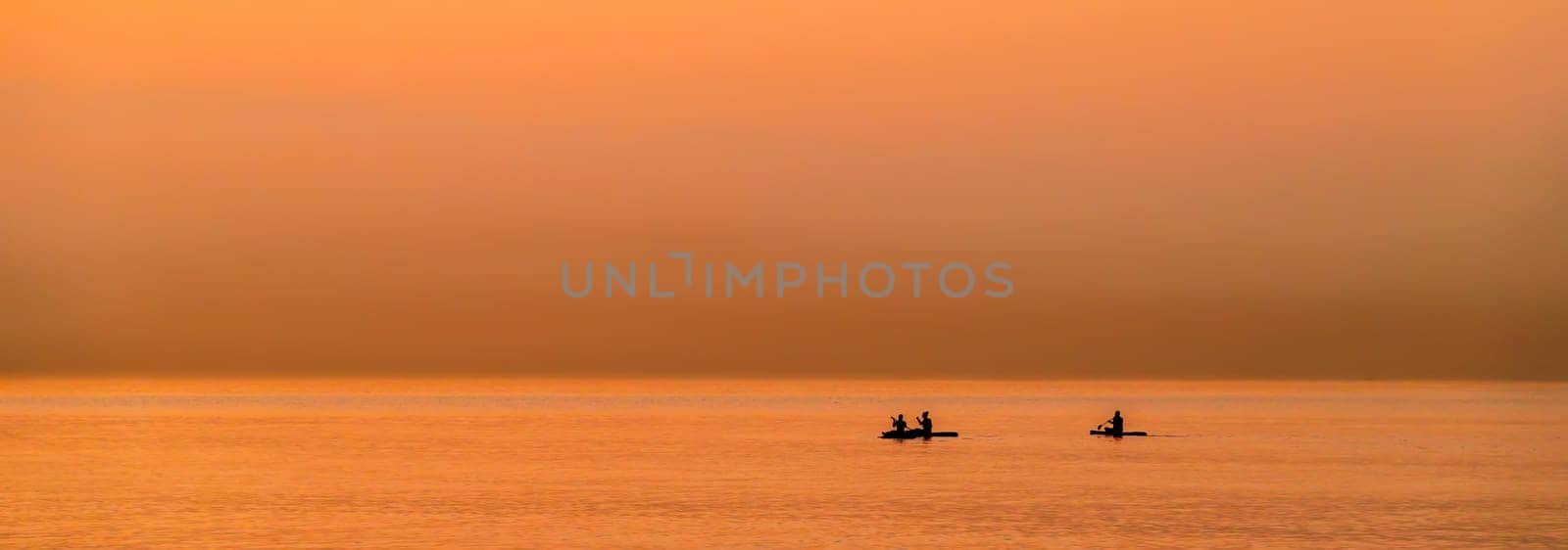 Adventurous people on a stand up paddle board is paddling during a bright and vibrant sunrise by Sonat