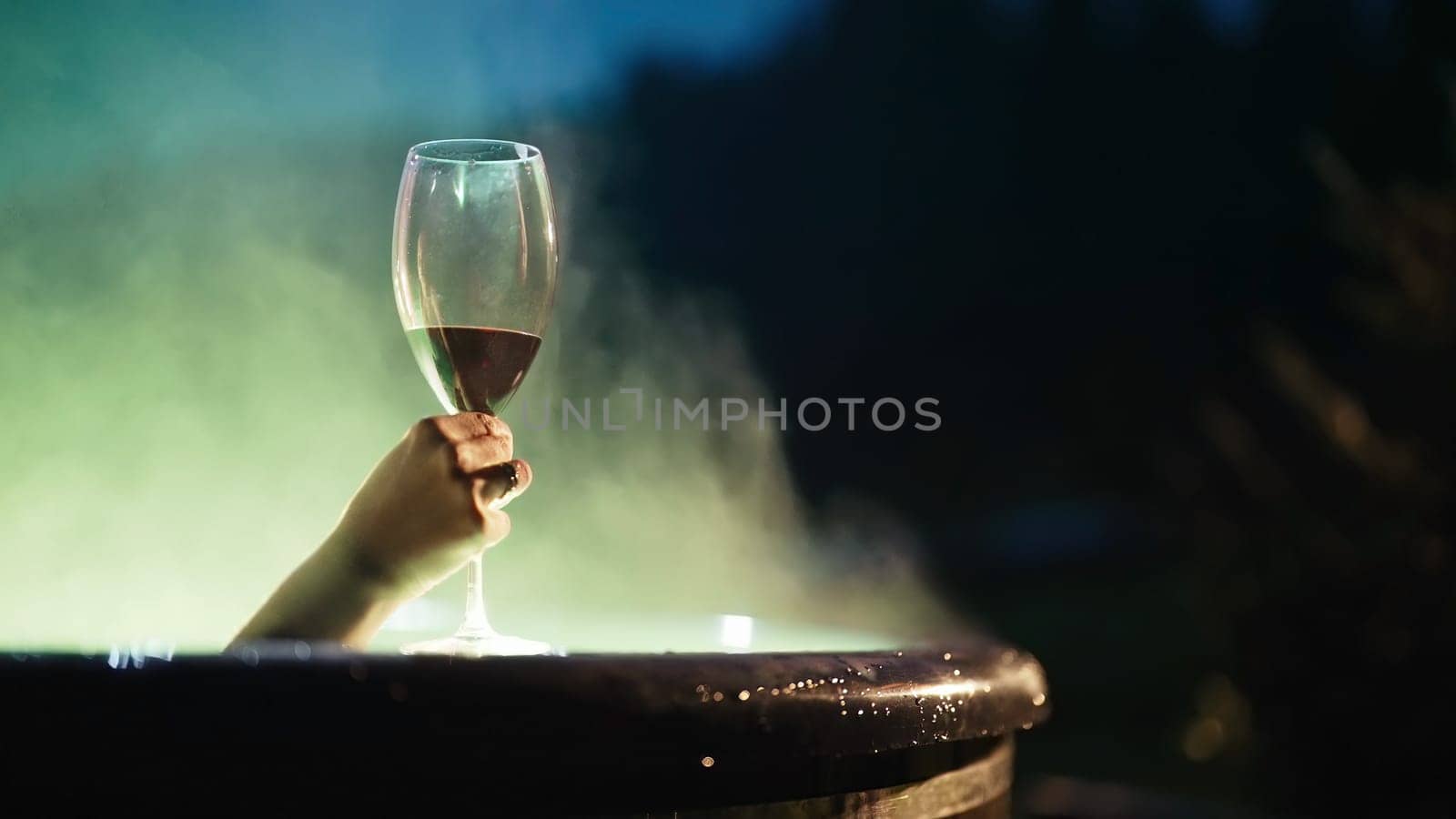 Woman spending holidays resting on wild nature, drinks red wine. Lady in hot wooden vat heated by firewood, bathing with mineral water. Aestethic footage. Eco living, wellness center, hydrotherapy.