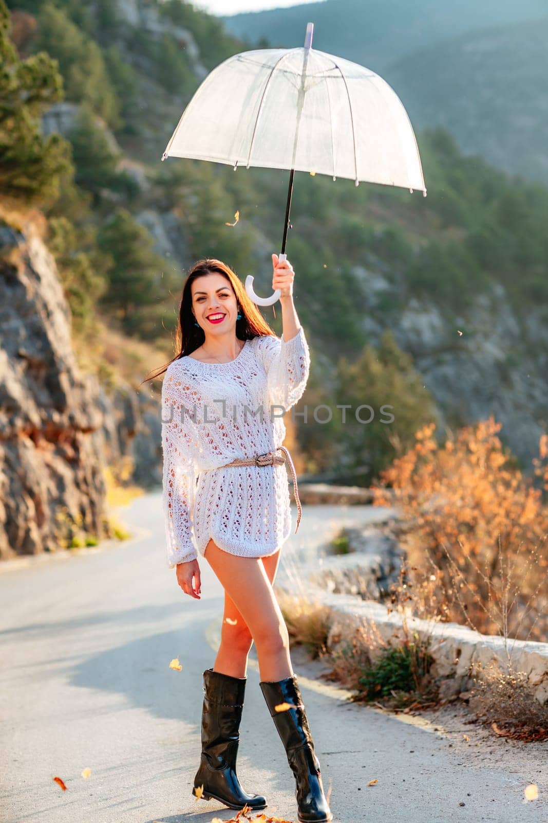 woman umbrella leaves , She holds him over her head, autumn leaves are falling out of him. Beautiful woman in a dress with an umbrella in the autumn park on the road in the mountains. by Matiunina