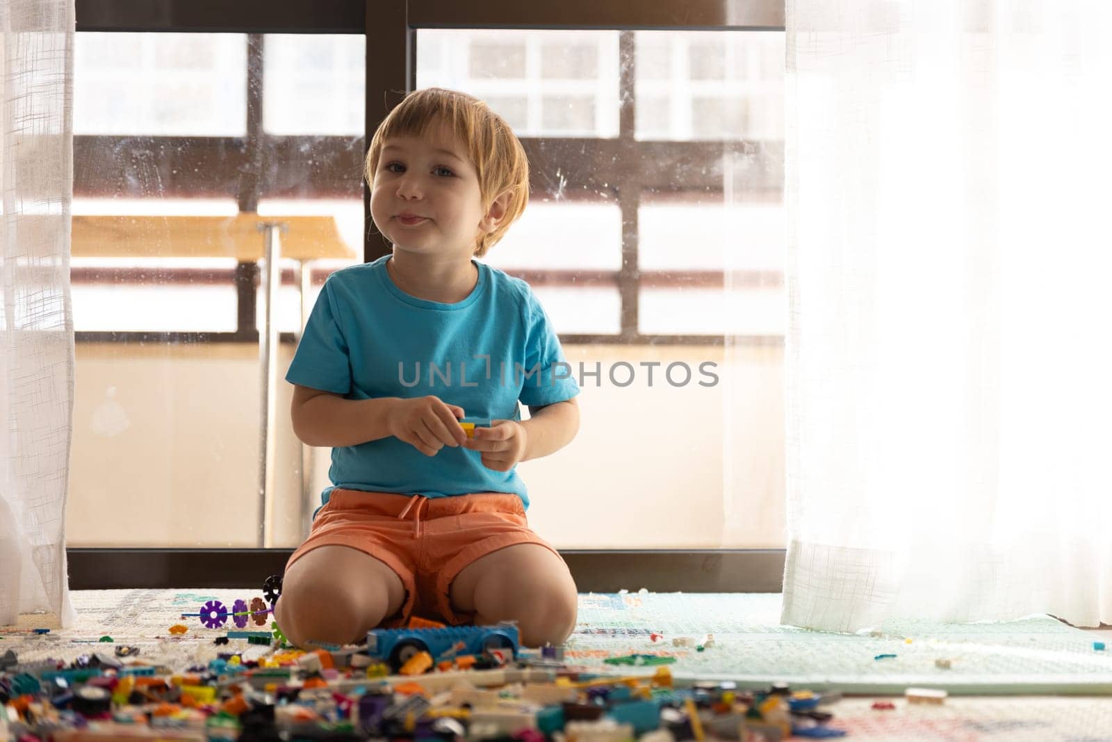 A little boy sitting on the floor in front of a window