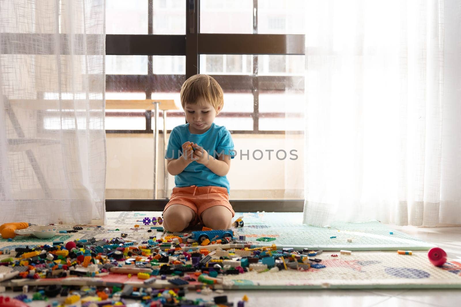 A little boy sitting on the floor in front of a window