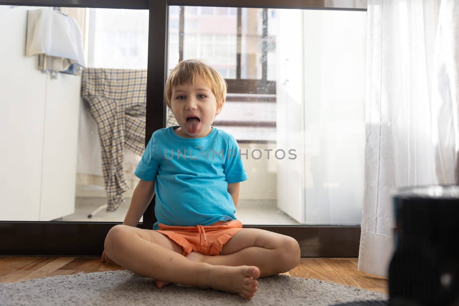 A little boy sitting on the floor making a funny face