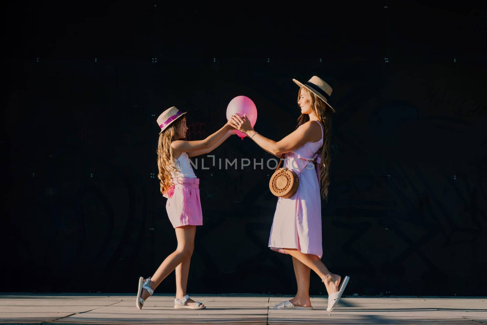mother and daughter stand in pink dresses with flowing long hair on a black background. Enjoy communicating with each other by Matiunina