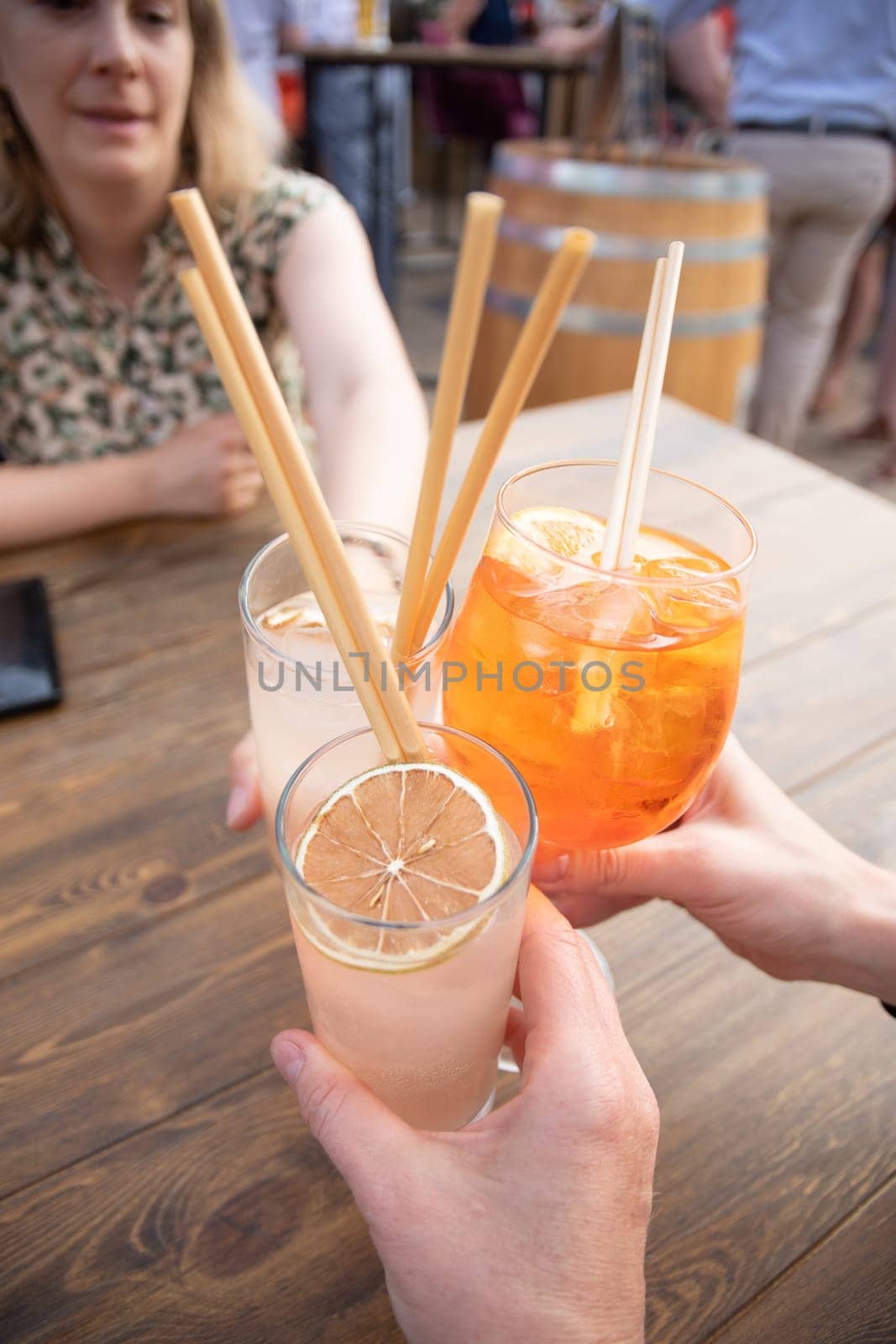 group of young girlfriends holding glasses with cold exotic cocktails sitting together at a table in the summer cafe by KaterinaDalemans