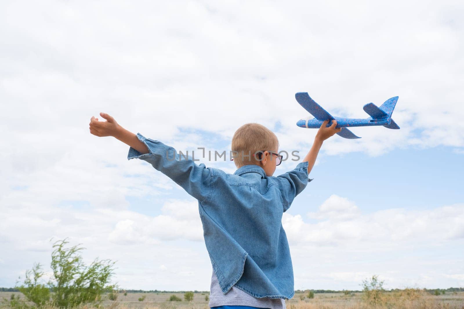 Happy child playing with a toy airplane against a blue sky in an open field by Ekaterina34