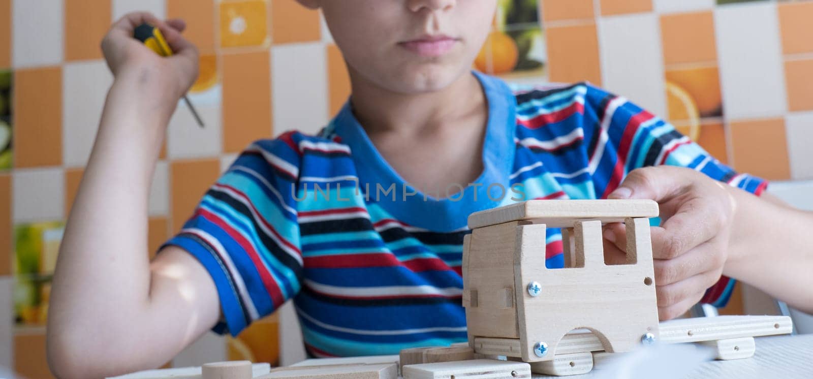 An 8-year-old boy assembles a wooden constructor by himself with a screwdriver. Close-up hands by Ekaterina34