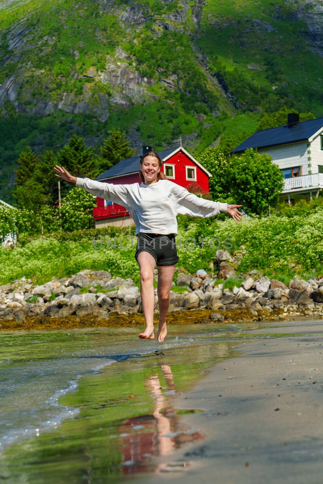 Young girl teenager running on beach in Norway Fjord. Vacation in Nordland in summer by PhotoTime