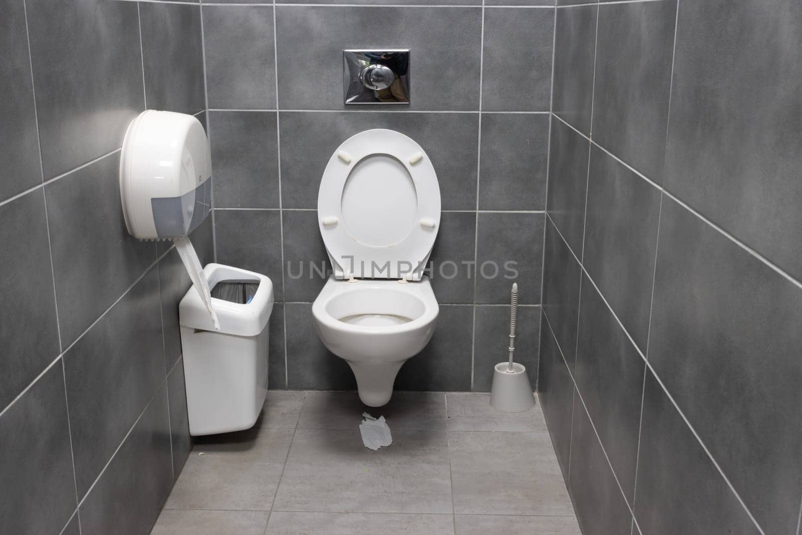 White toilet and trash can in a gray restroom. Mid shot