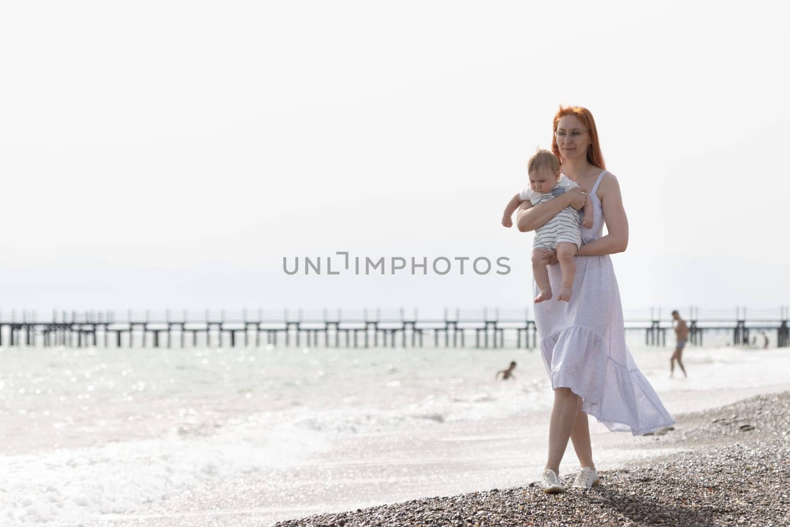 Mother walking on a beach with her little son. Mid shot
