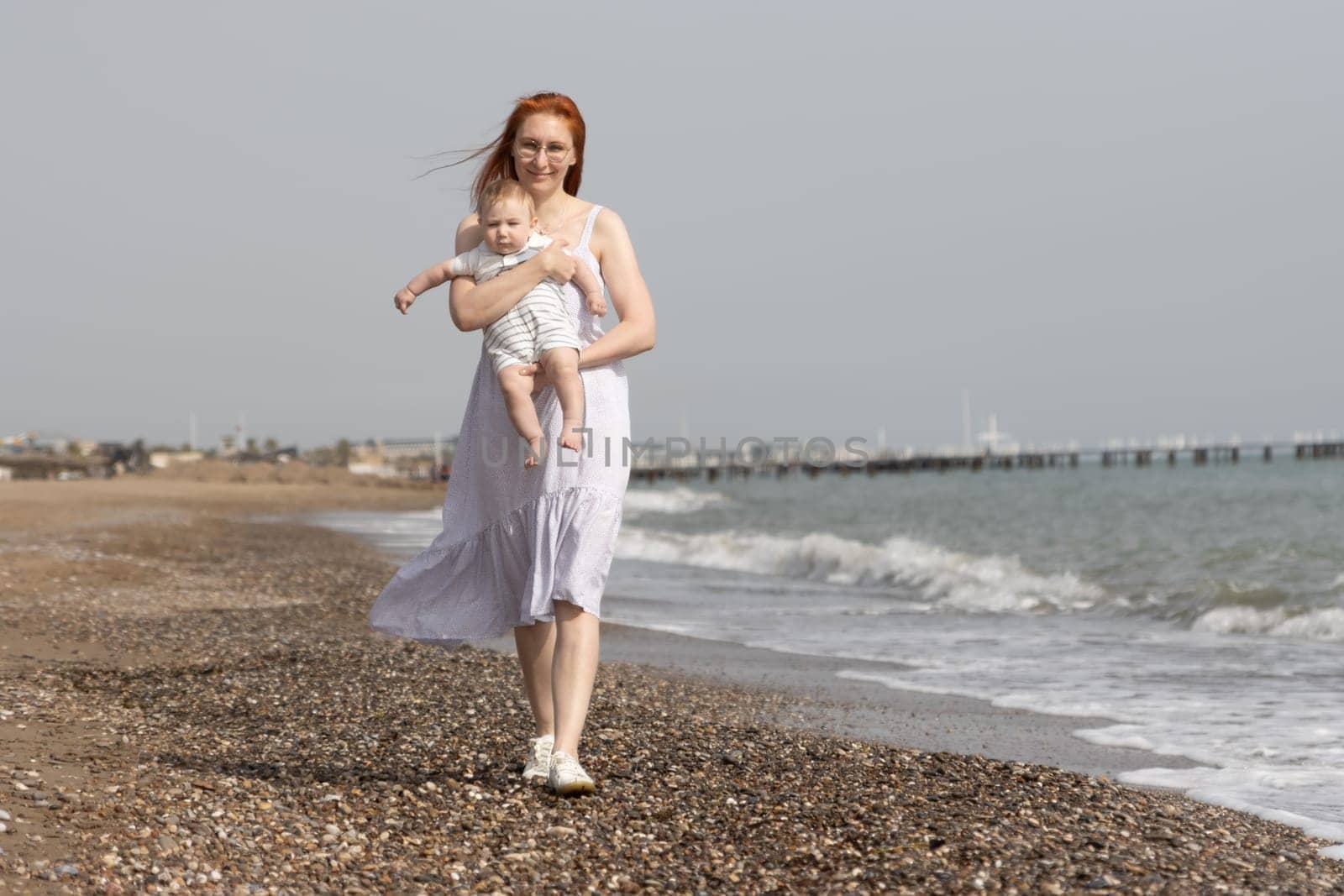 Mother walking on a beach with her little son on her hands by Studia72