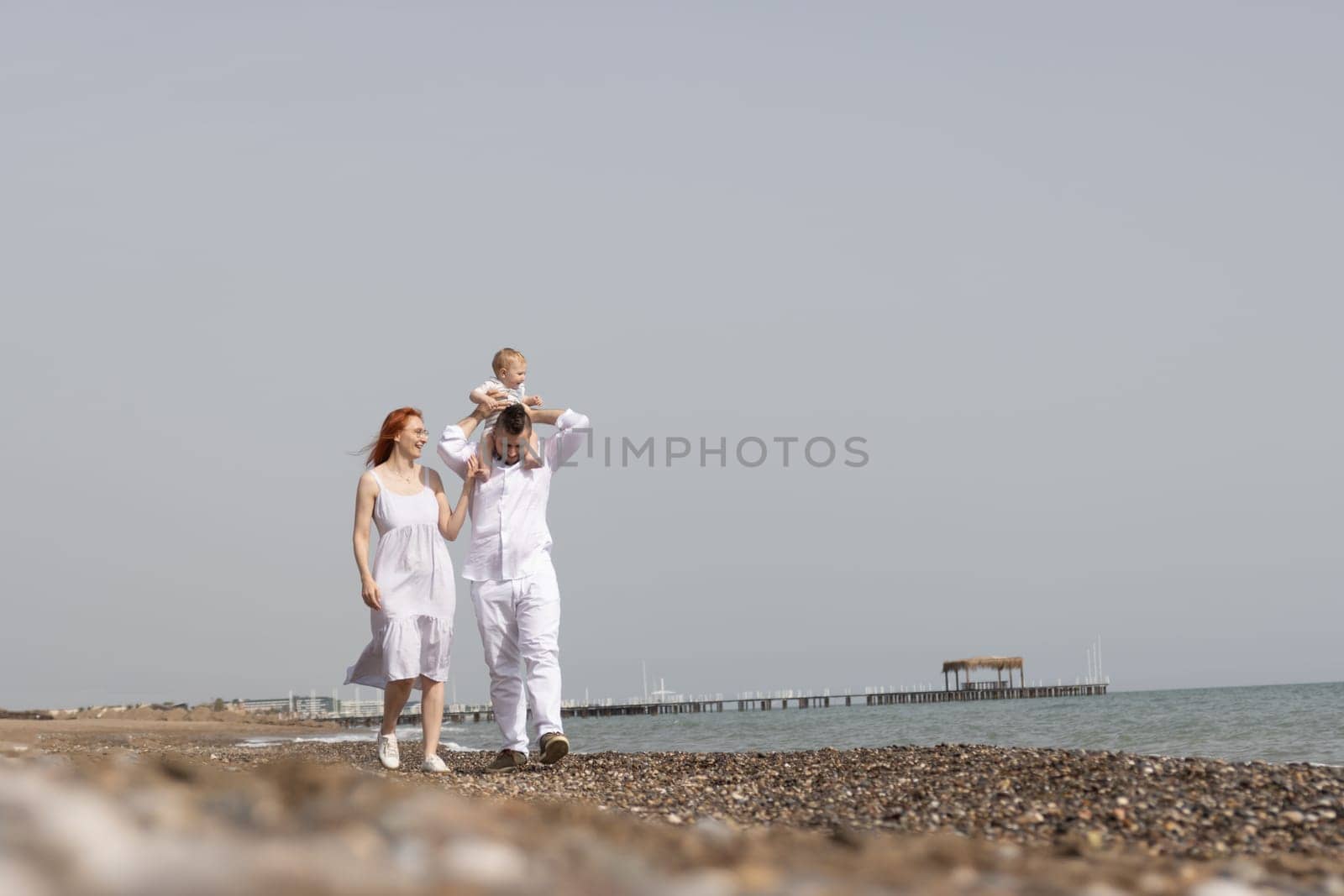 Happy family with little son on father's shoulders walking on a beach by Studia72