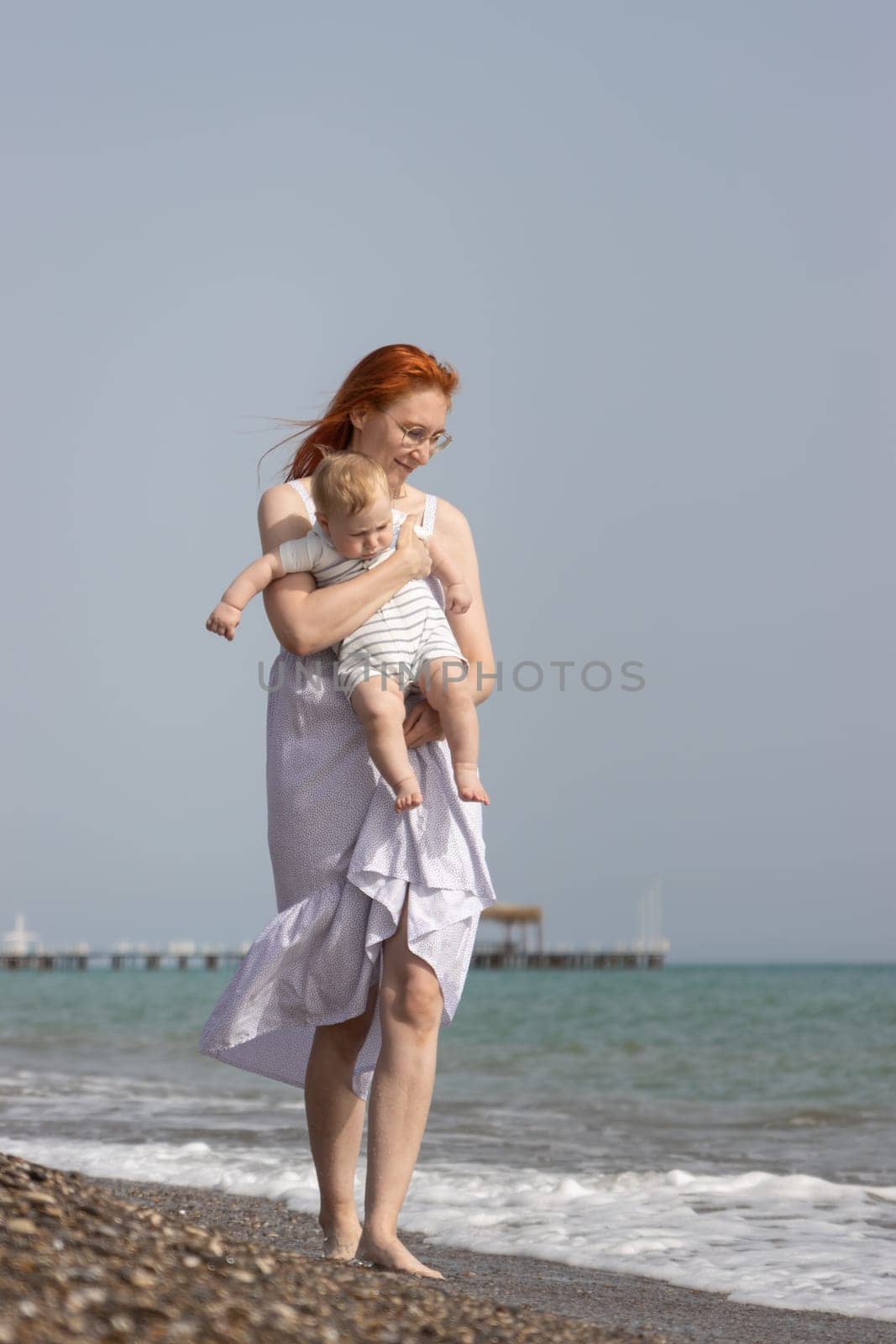 Smiling woman walking on a beach with her little son. Mid shot