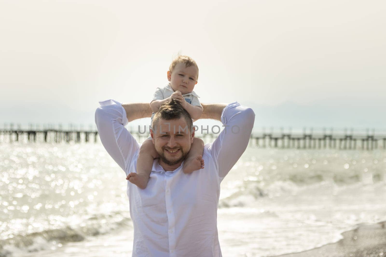 Happy father on vacation - smiling man holding his little baby son on his shoulders by Studia72