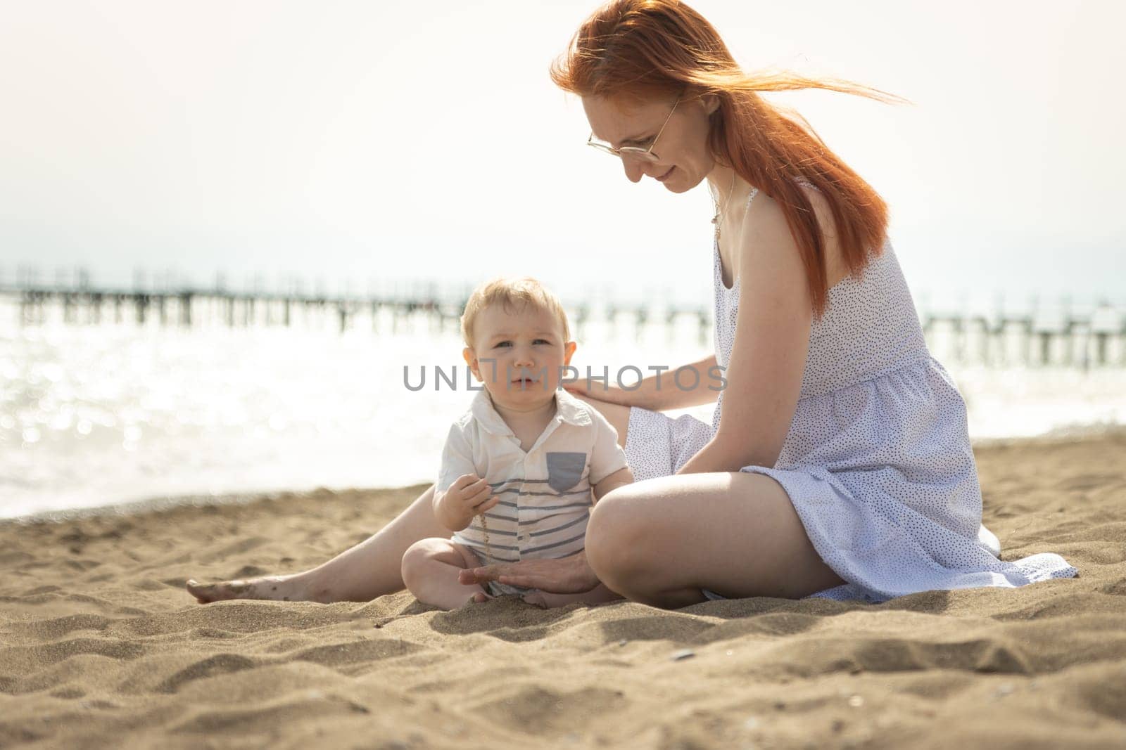 Happy mom playing with sand with her little baby son. Mid shot