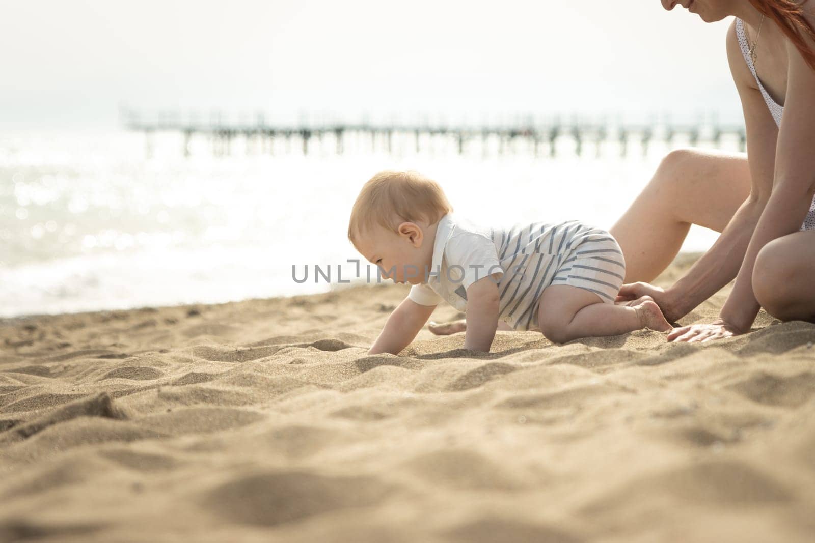 A little baby boy crawling on a sand on the seaside. Mid shot