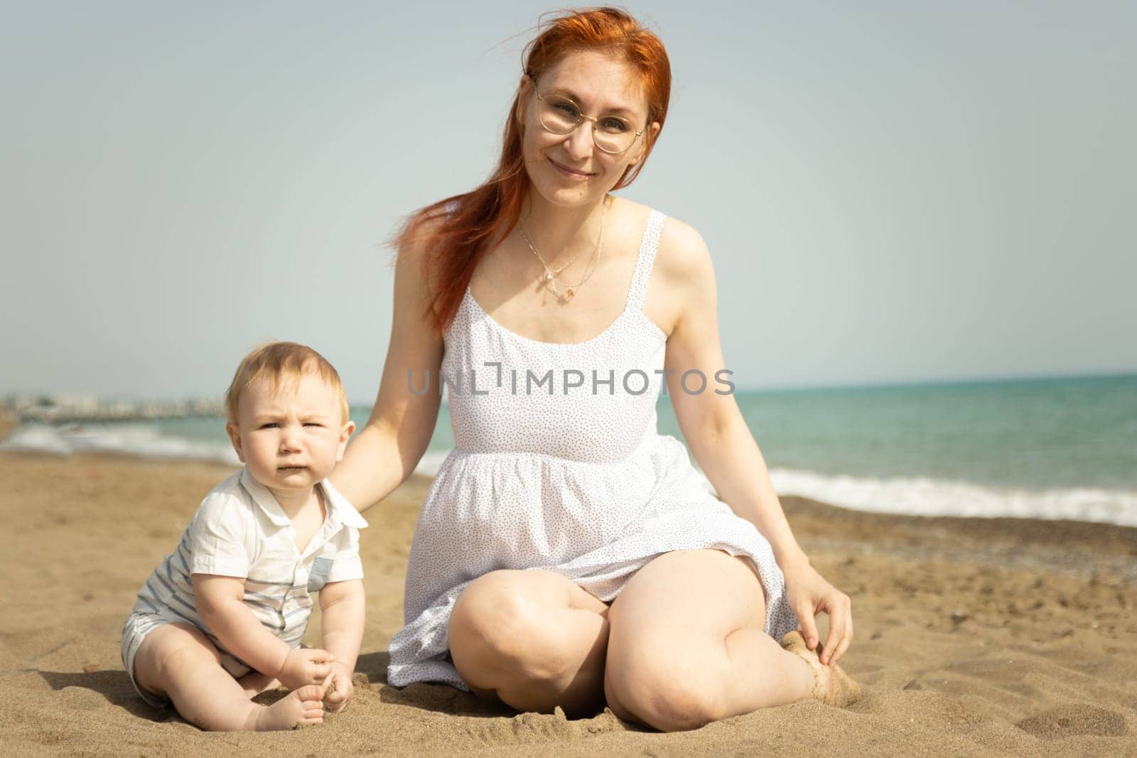 Happy mom with her little baby son on the sand beach. Mid shot