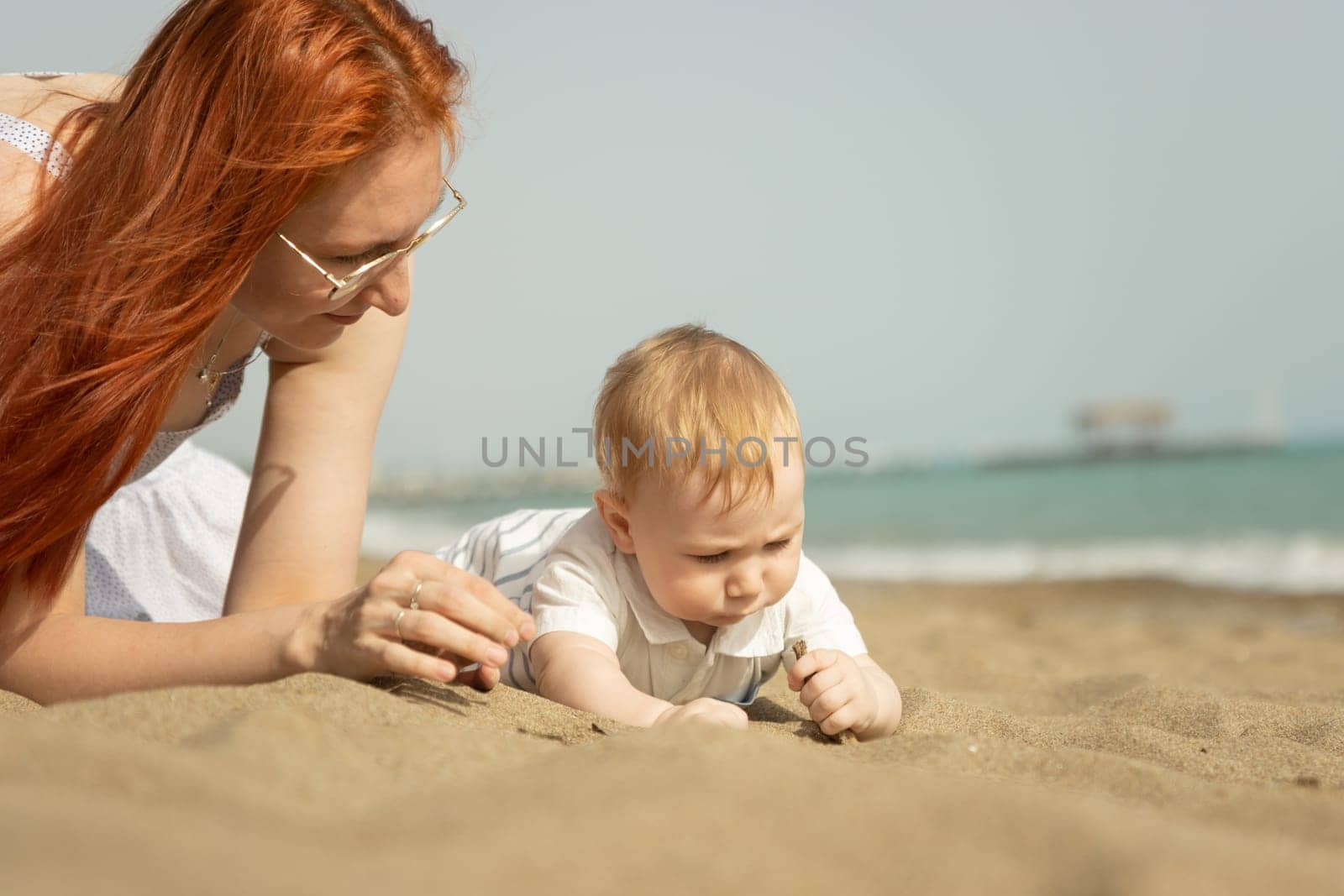 Mother playing with sand with her little baby son. Mid shot