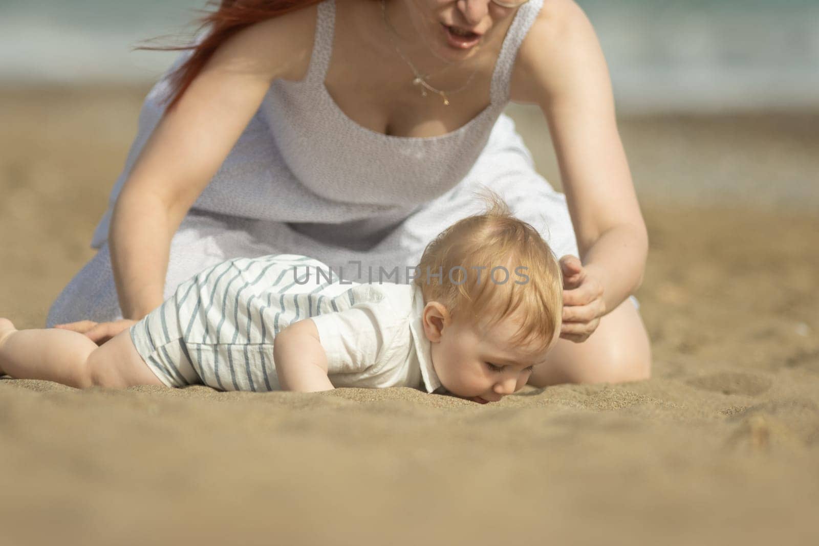A little boy trying to eat the sand and his mother stopping him. Mid shot