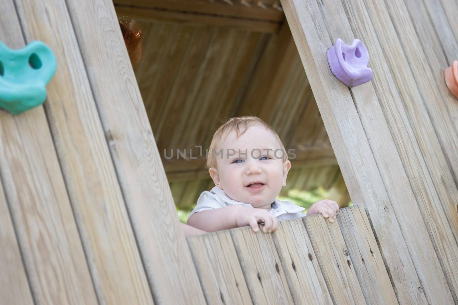 Funny baby sits in a wooden house on the playground by Studia72