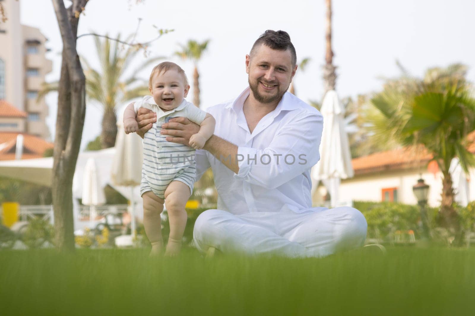 Happy father and his cute son sit on the grass - looking into the camera by Studia72